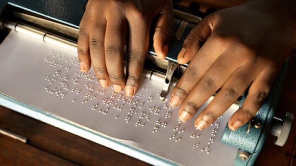 A close-up of a girl's hands as she reads from a braille document.