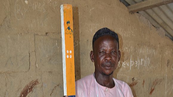 Saadu stands with a measuring stick.