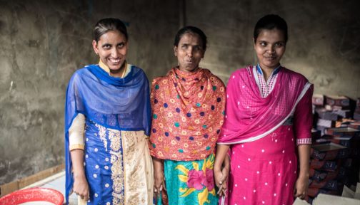 Three women wearing saris stand together smiling.