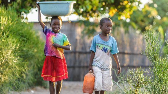 Namukolo och hennes bror bär vattenhinkar genom byn där de bor.