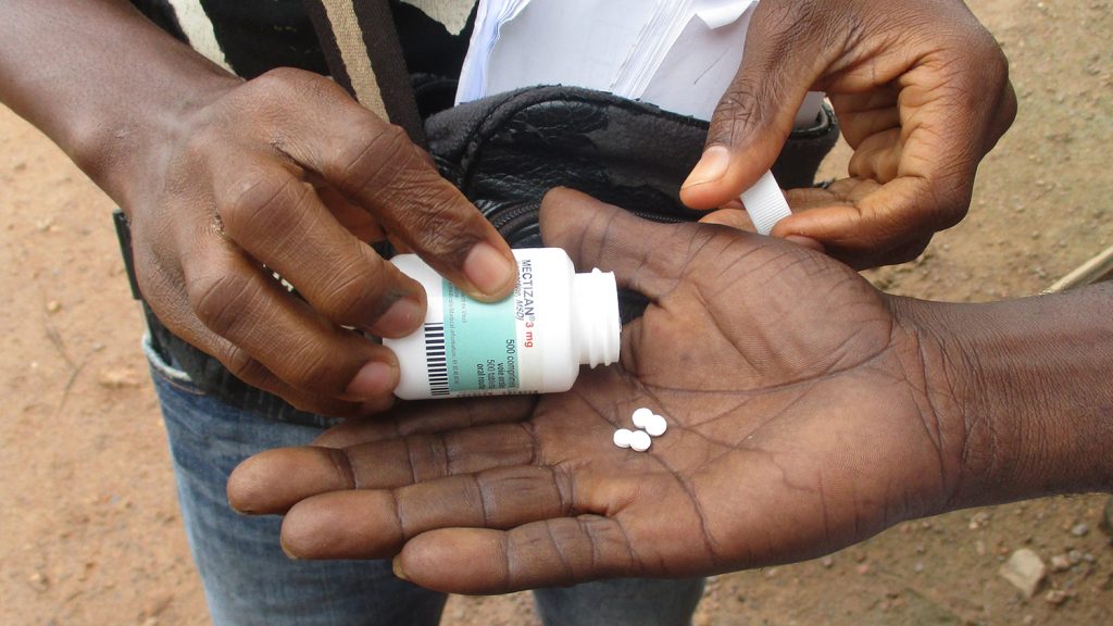 En volontär lägger medicin i handen på en man.