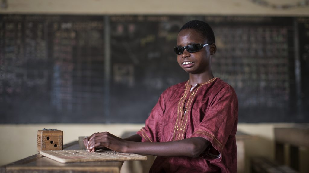 En ung pojke läser blindskrift i ett klassrum.