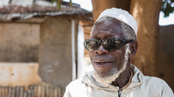 A male trachoma patient sitting outside, smiling.