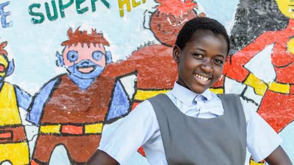 Skolelever ler framför en väggmålning i Zambia.