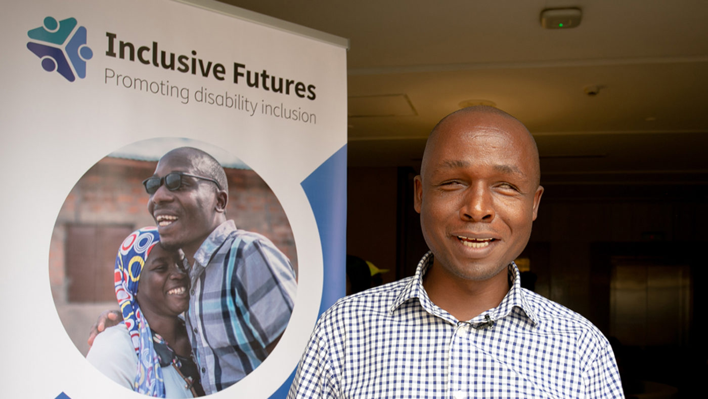 Deus Turyatemba står bredvid en Inclusive Futures-plansch