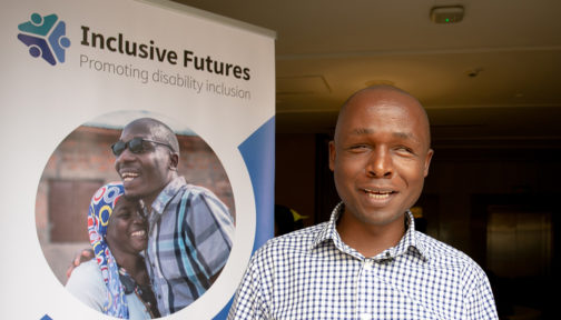 Deus Turyatemba står bredvid en Inclusive Futures-plansch