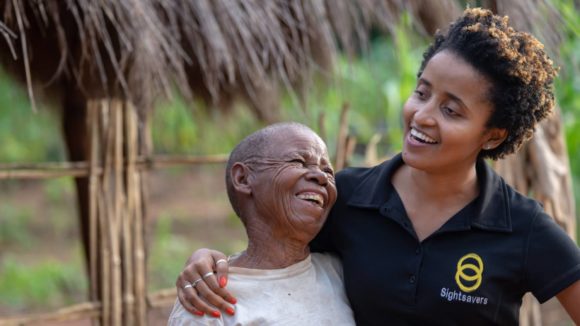 Mercia laughs and celebrates with a trachoma surgery patient after her bandages have been removed.