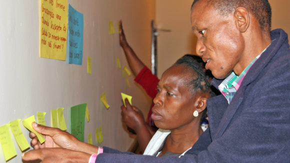 Two people reading notes on a wall during a workshop.