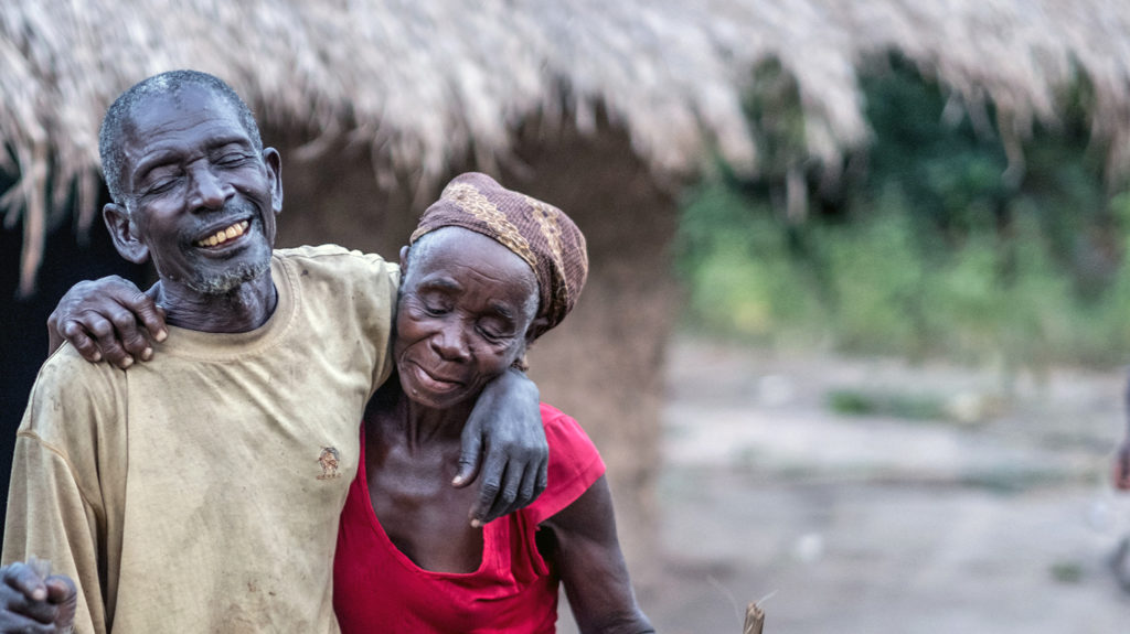 Gordane och Suhura håller om varandra och ler utanför sitt hem i Moçambique.