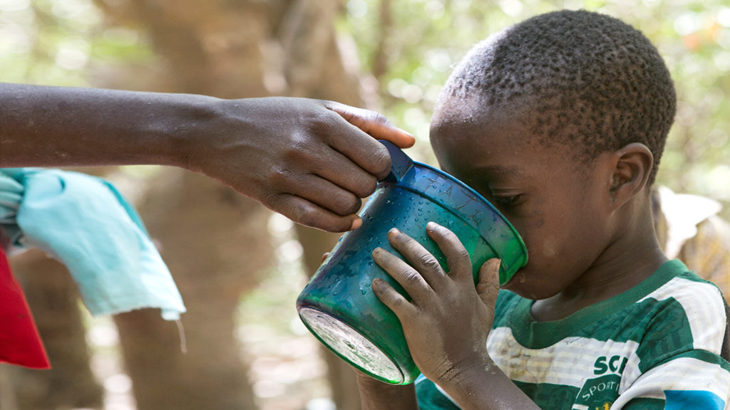 Ett barn dricker vatten ur en mugg under en kampanj för distribution av läkemedel i Nigeria.