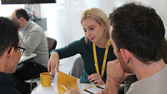 En grupp kreativa personer sitter vid ett bord och diskuterar sin uppgift.