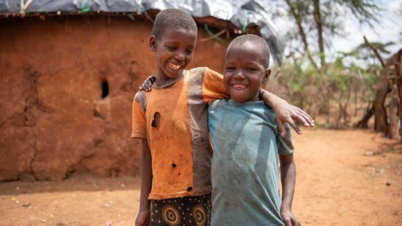 Noomi och Rakonin, unga flickor, stod utanför och log med armarna om varandras axlar.
