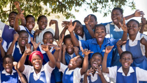 En stor grupp skolelever i Malawi. De är klädda i klarblå uniformer och har samlats utanför, ler och jublar.