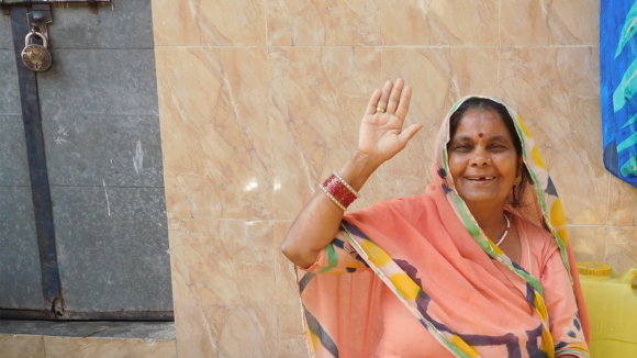 A woman smiles and waves at the camera.