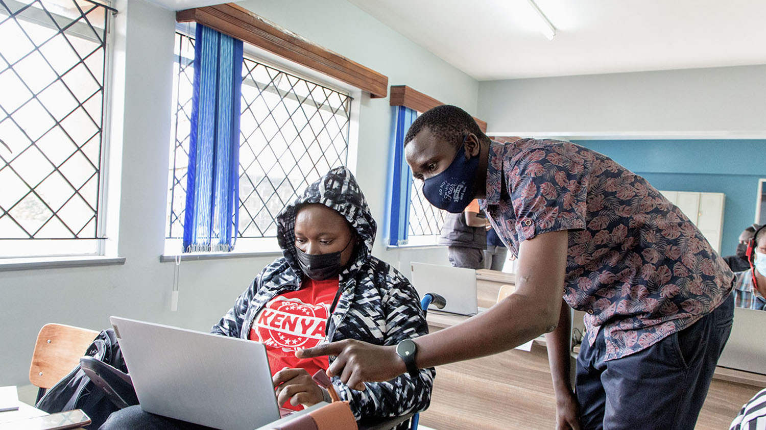 I ett klassrum får en elev i rullstol undervisning av en lärare.